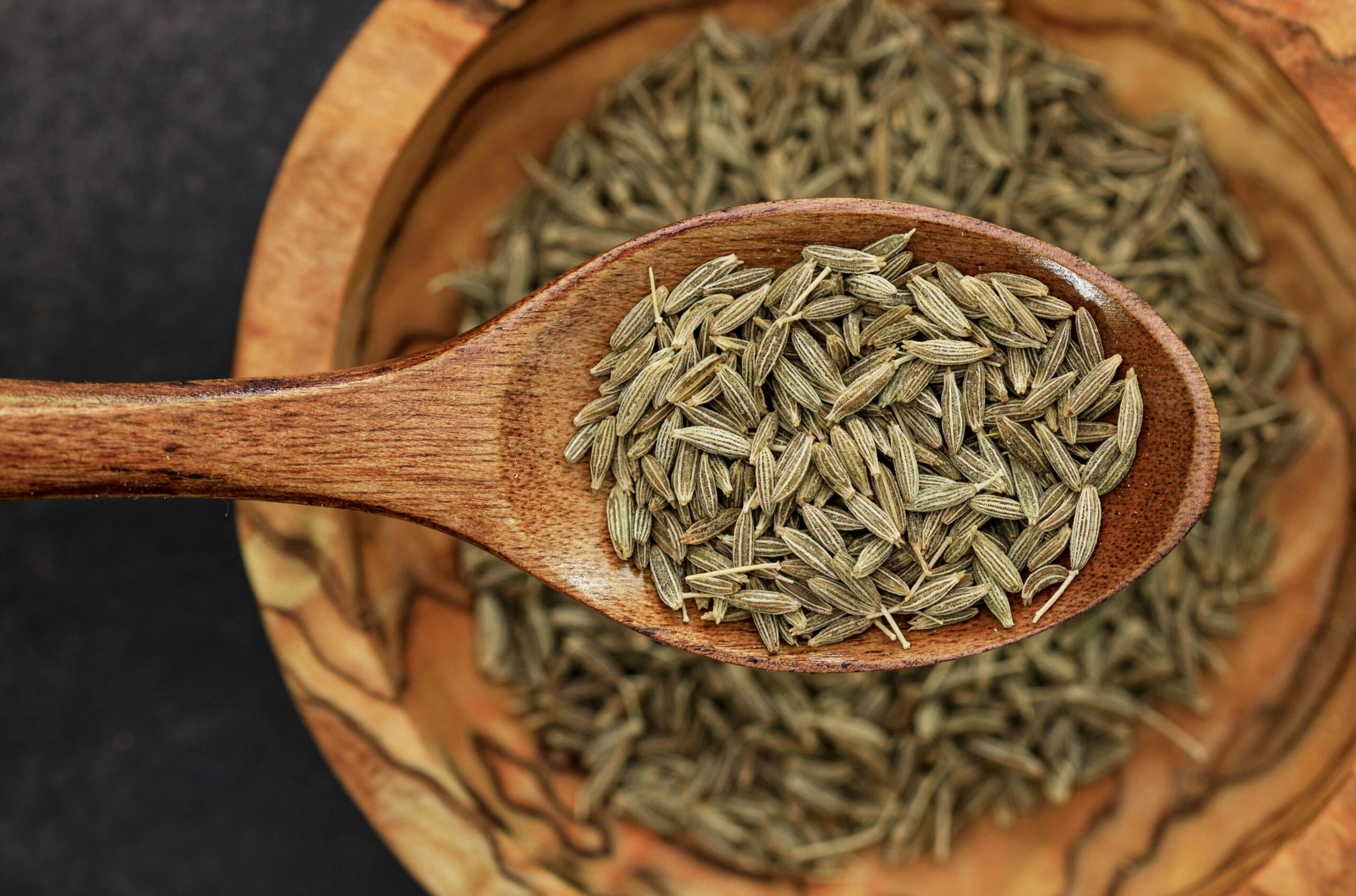 Detailed image of cumin seeds on a wooden spoon for culinary use.